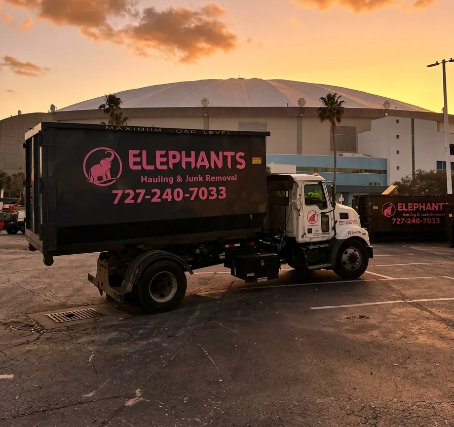 Elephants Hauling & Junk Removal truck delivering a roll-off dumpster at Tropicana Field in St. Petersburg FL at sunset